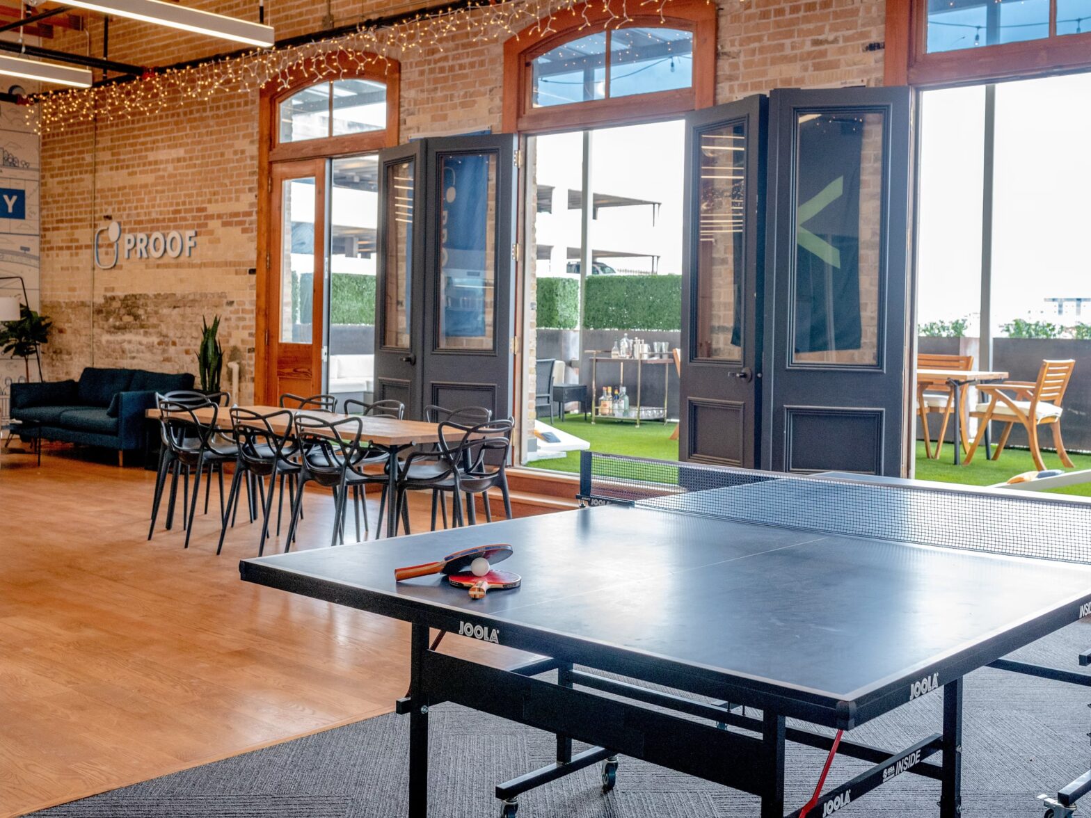 Sala común de oficina con sofá negro, sillas de diseño y grandes ventanales con vista urbana